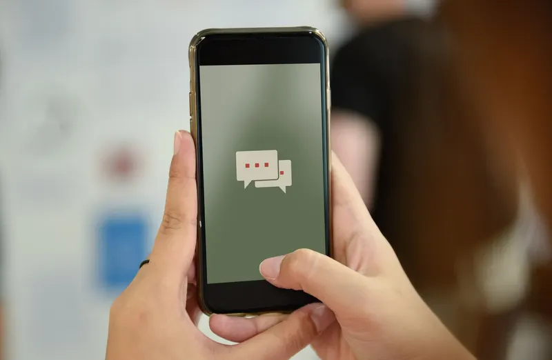 Person typing in a chat window on a smartphone beside a laptop keyboard