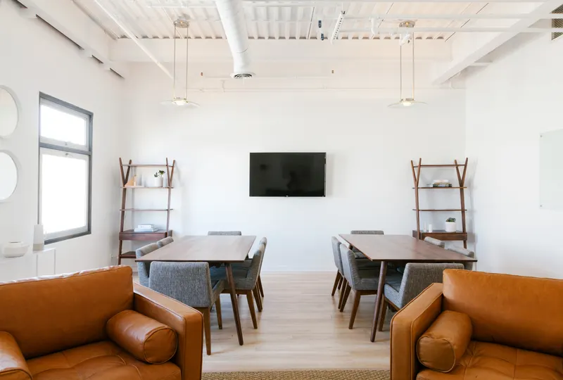 Modern office meeting room with two tables, a wall-mounted display and leather lounge seating