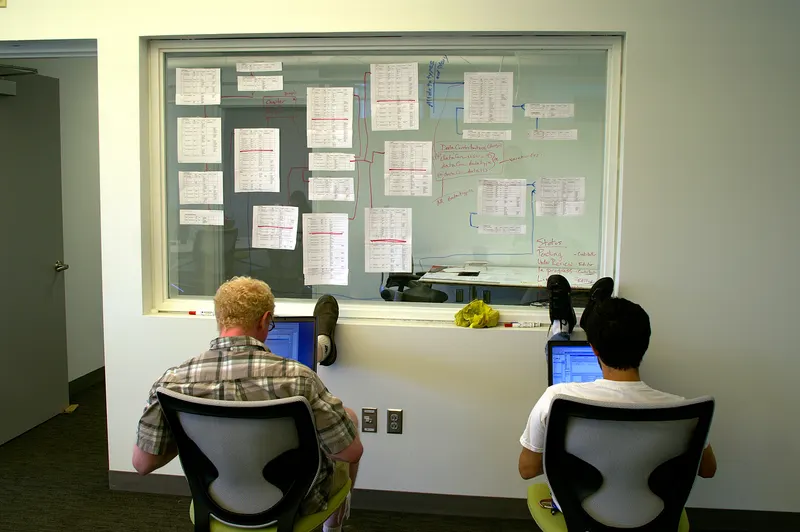 Consultant mapping a workflow with sticky notes across a glass office wall